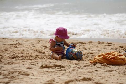 A child wearing a hat playing with the send in the beach