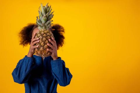 girl hiding her face behind a pineapple 