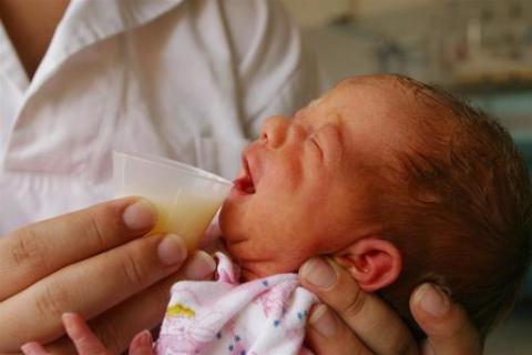 baby being fed with breastmilk from a cup