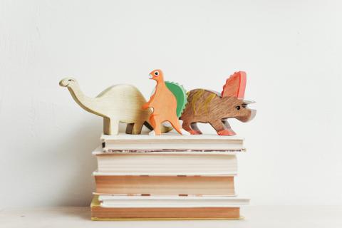 three wooden dinosaurs on books