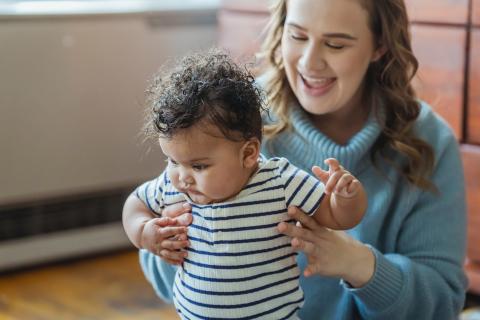 mother supporting baby standing in front of her